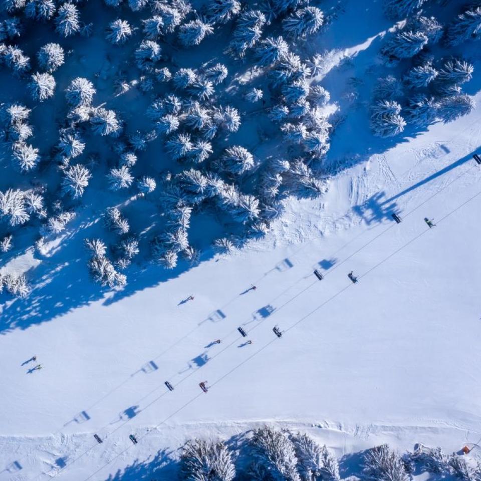 Aerial view of a ski lift in Kopaonik, with skiers descending the hill on a winding slope alongside snow-tipped trees