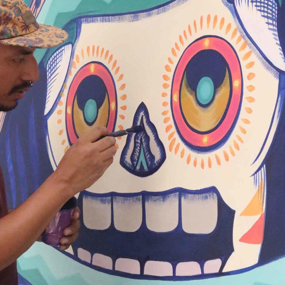 A man paints a colorful skull mural outdoors at Awacate restaurant