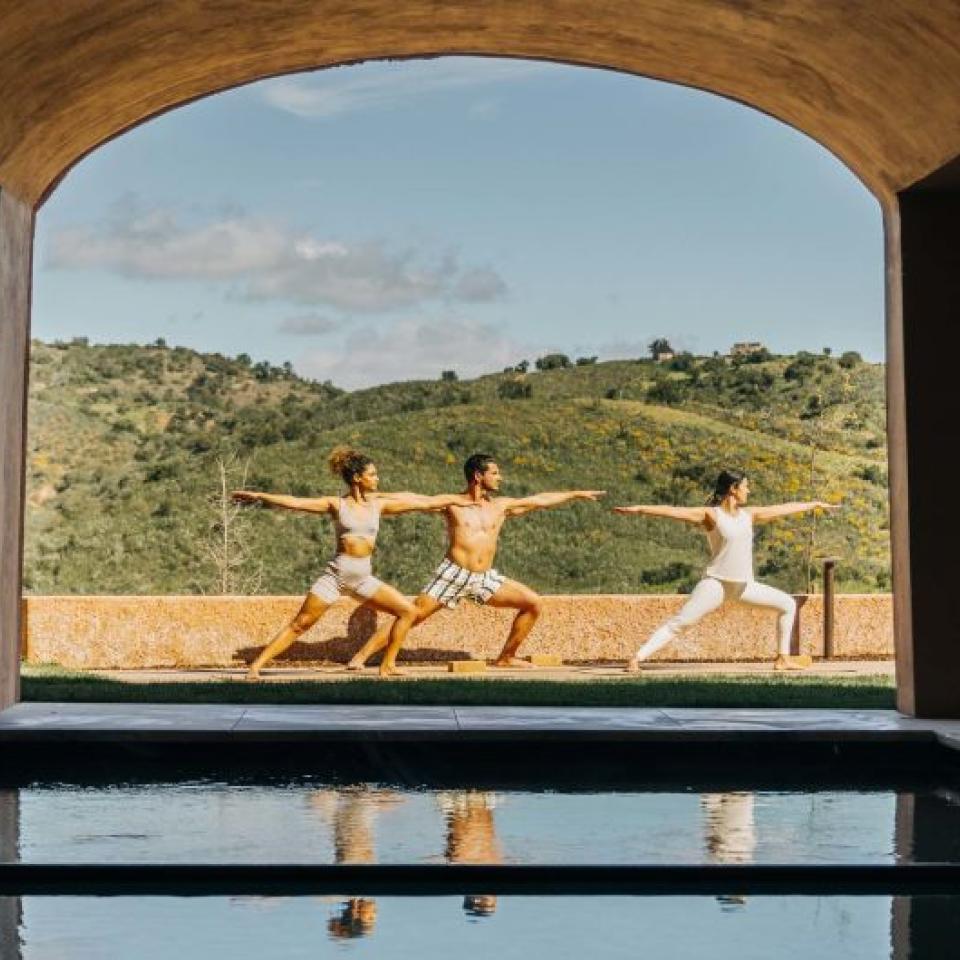 Three people doing yoga in a spa courtyard at Viceroy Ombria Algarve, with rolling hills in the background