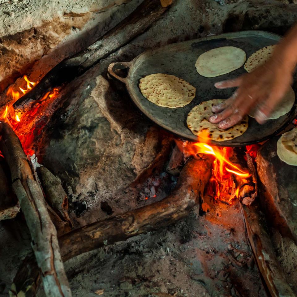 A hand pressing tortillas onto a cast iron pan over flames.