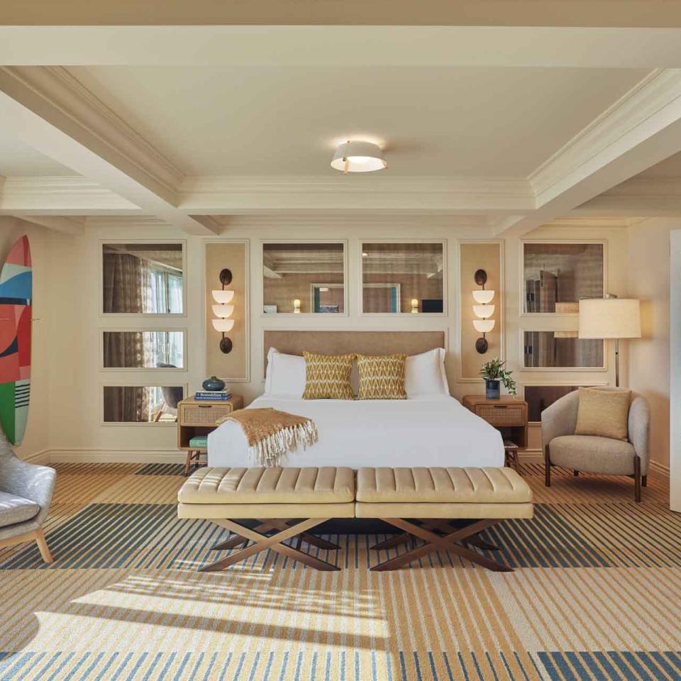 A King Bed in a large suite, with an arm chair and a surfboard mounted on the wall