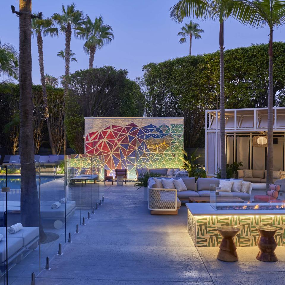 An outdoor gathering space with couches around a fire pit and cabanas surrounding a pool