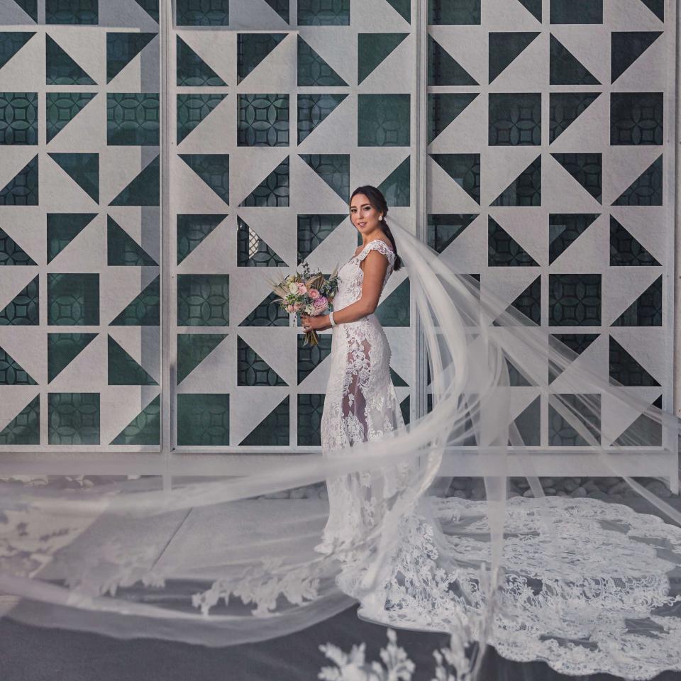 A bride poses with her bouquet next to a concrete mosaic wall