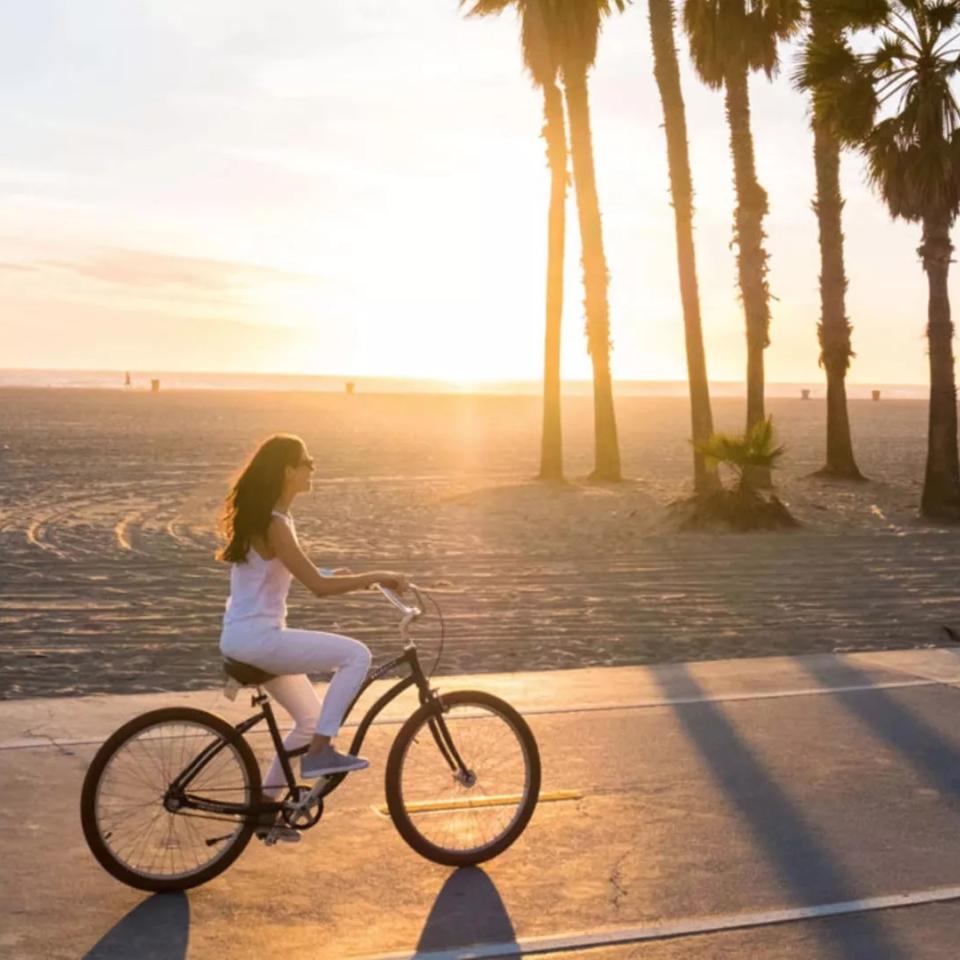 A woman rides a bike along Santa Monica beach at sunset