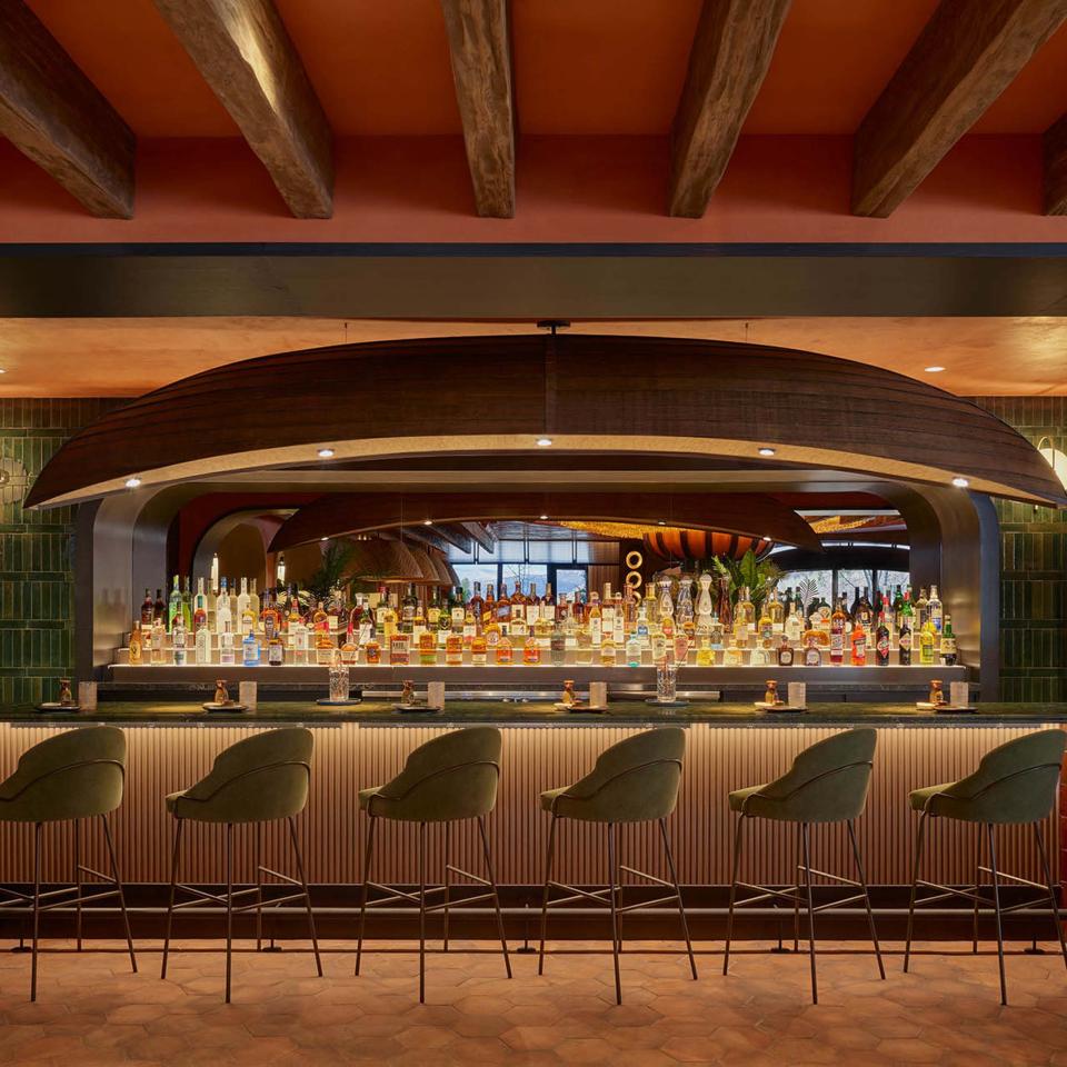 The bar at Cafe V, featuring a row of stools and a full-service bar counter, surrounded by greenery