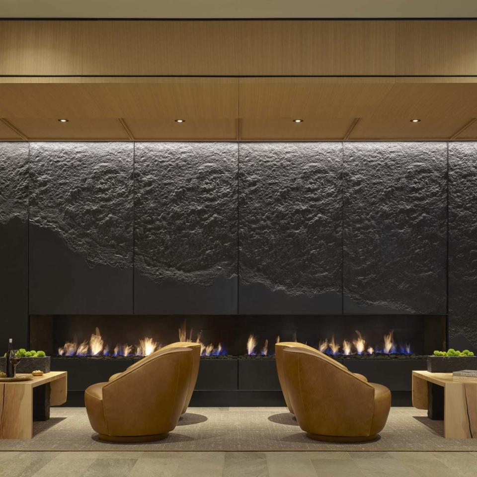 A cozy lobby seating area at Viceroy Snowmass, with chairs across from a large stone fireplace