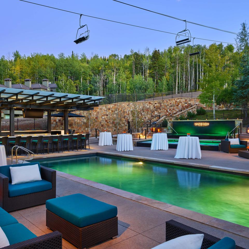 An outdoor patio surrounding a wading pool with linen-topped banquet tables, with a ski lift overhead and mountainous trees in the background