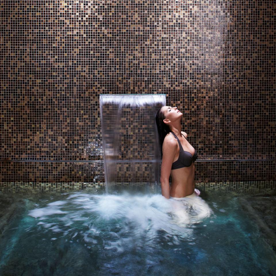A woman wading in a spa pool and washing her hair with a rain shower