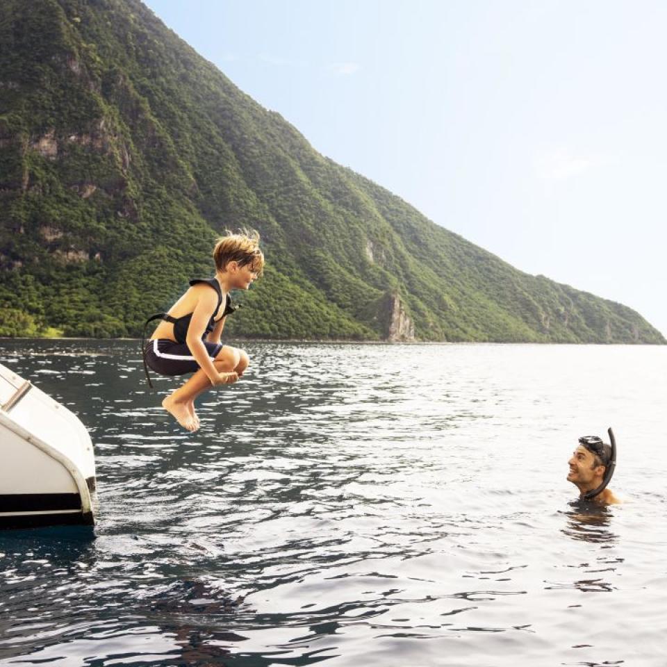 A child jumps from a boat as his father awaits in the water, near Sugar Beach with the Pitons in the background