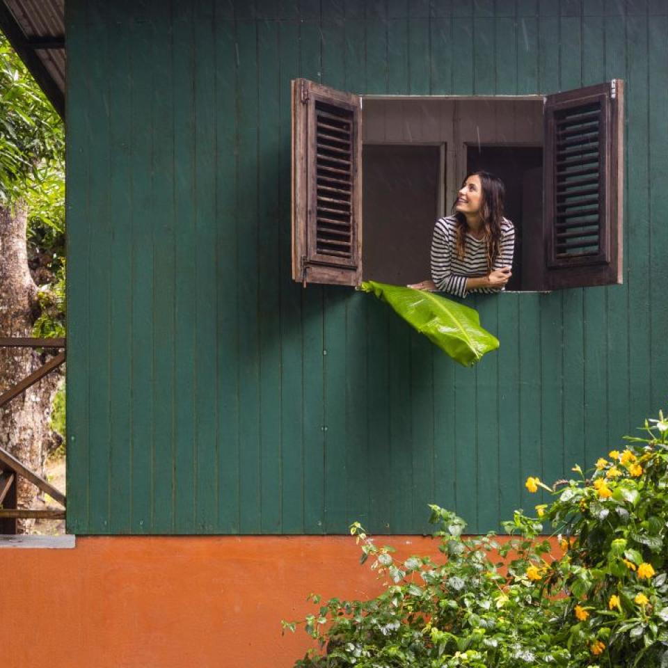 A woman looks out the gabled window of a green residence at the tropical greenery surrounding her, at Viceroy Sugar Beach