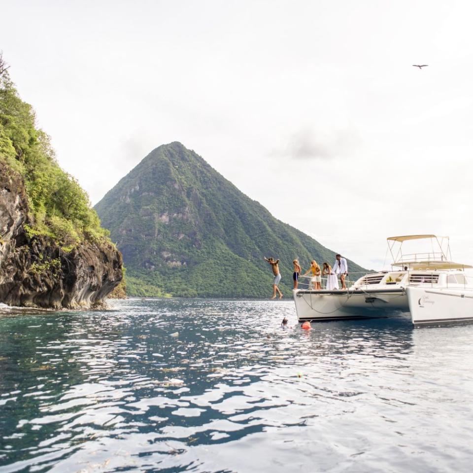 Friends jump into the water off a yacht anchored near Sugar Beach, in view of the Pitons