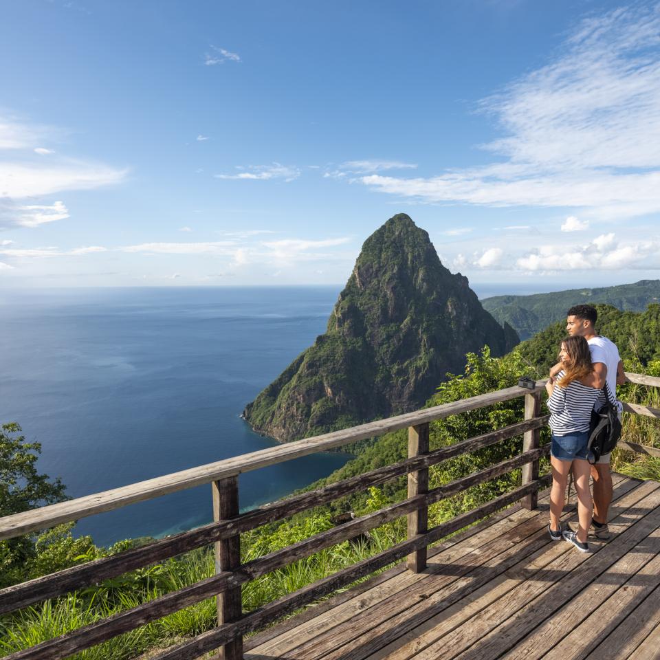 A couple looks out at the ocean and a tropical mountain from a viewing platform atop a ridge