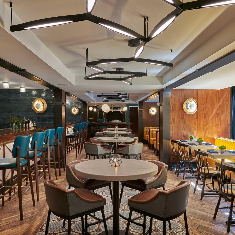 The dining room of Dovetail restaurant at Viceroy Washington DC, with a row of yellow booths adjacent to a long bar seating area