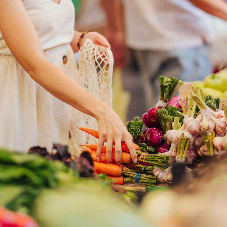A woman grabbing a bundle of carrots from a vegetable stand