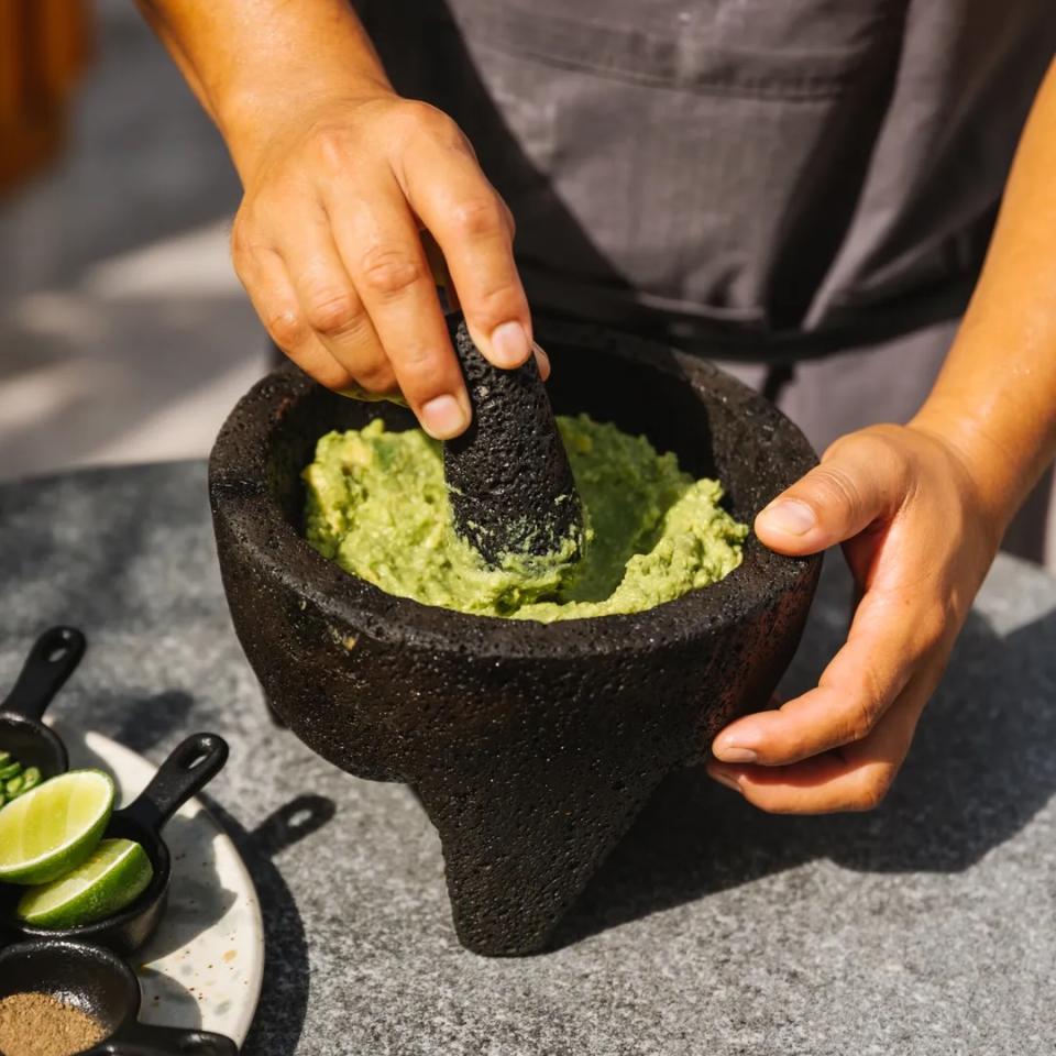 A man makes guacamole in a stone molcajete