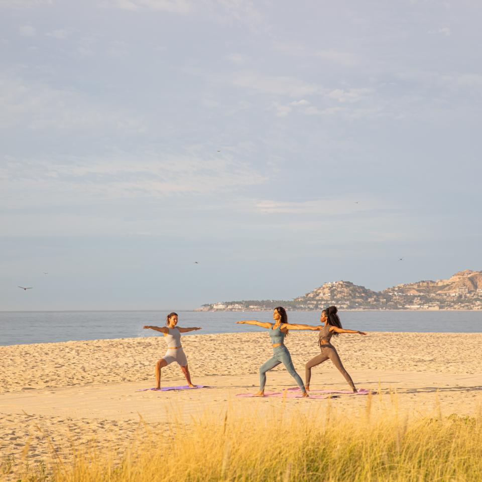 three people in yoga pose on beach
