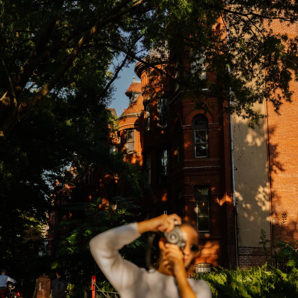 A woman takes a snapshot as she walks a residential neighborhood.