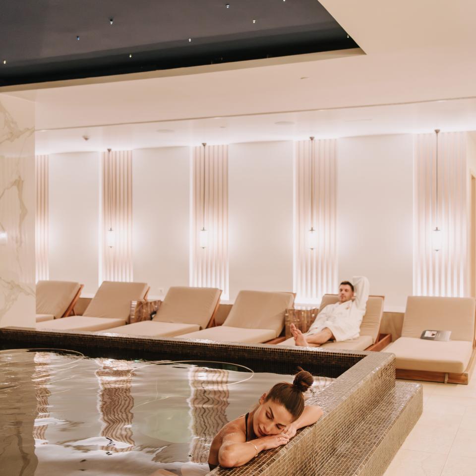 Un couple se détend dans un spa luxueux doté d'une piscine et de transats, sous un plafond étoilé.