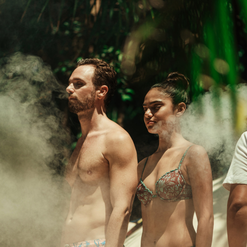 Un homme et une femme en maillot de bain se tiennent debout dans un épais brouillard, avec une végétation luxuriante en arrière-plan.