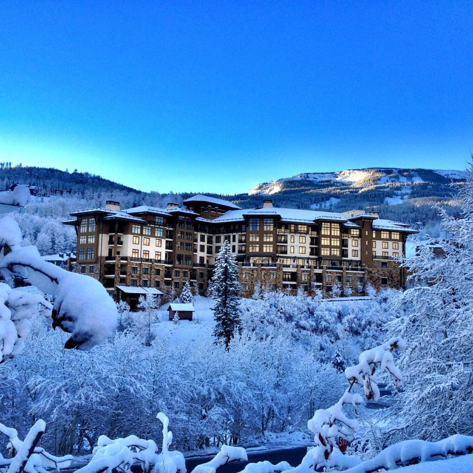 A large, modern ski lodge nestled on a snow-covered mountainside under a clear blue sky.