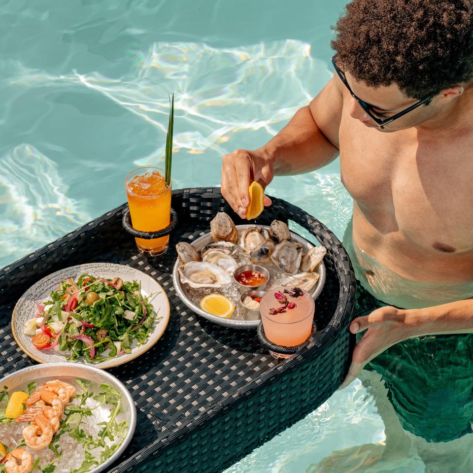 A man eating oysters and other snacks on a floating tray in a pool