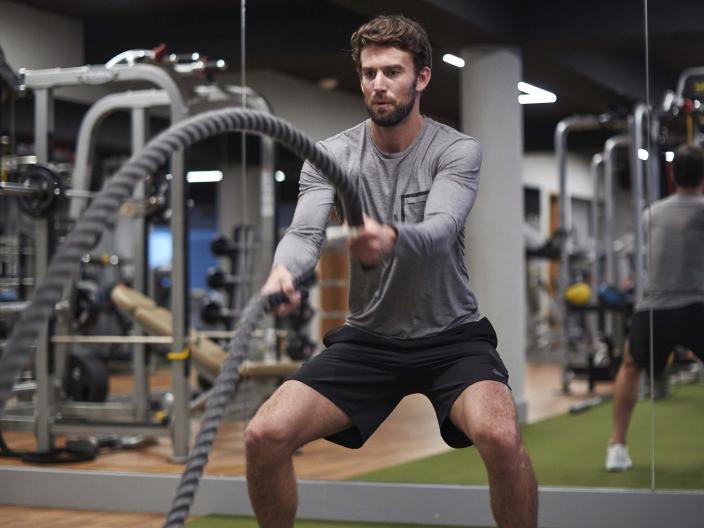man in gray shirt and black shorts stands on turf holding ropes
