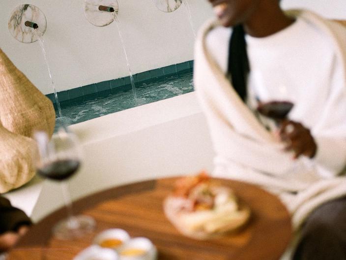 woman in white sits at wooden table with plates of food