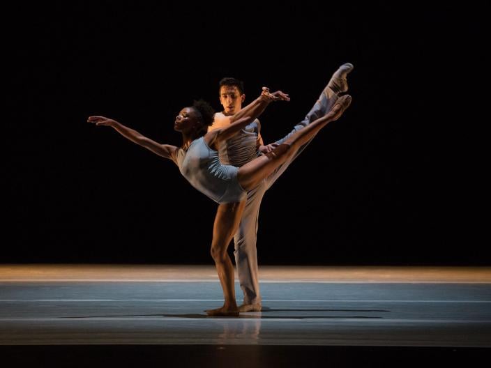 two ballet dancers pose in the middle of a darkly lit stage
