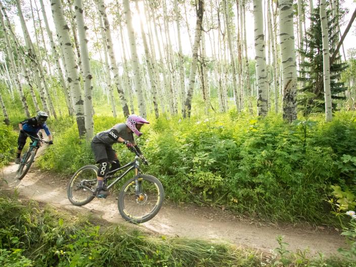 two people on mountain bikes race through wooden trail
