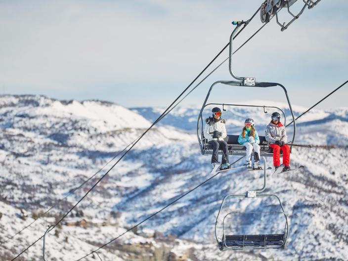 group of skiiers on chairlift with snowy mountains in background