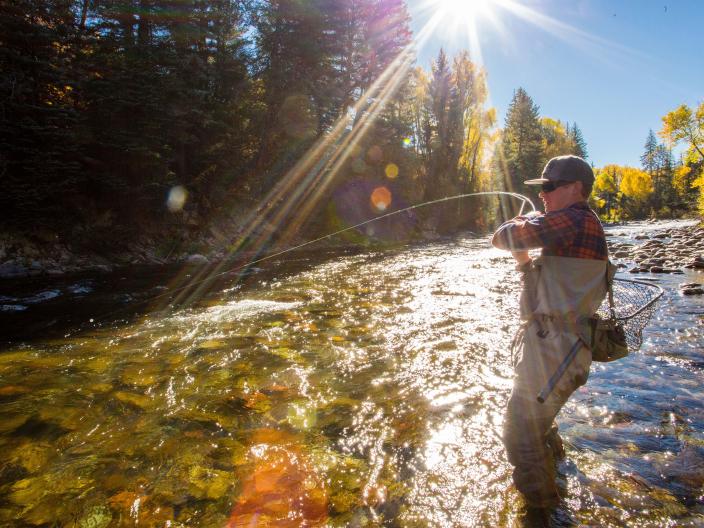 person fly fishing in river with sun shining in background