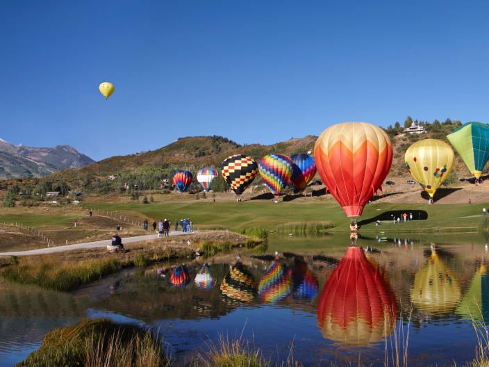 cluster of hot air balloons in a field near a body of water