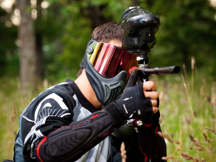 person in paintball safety gear points paintball gun towards camera