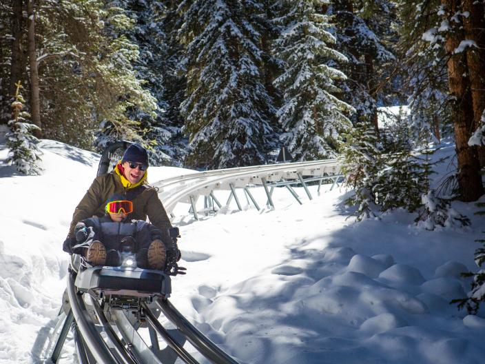 two people ride alpine coaster through snowy tree area