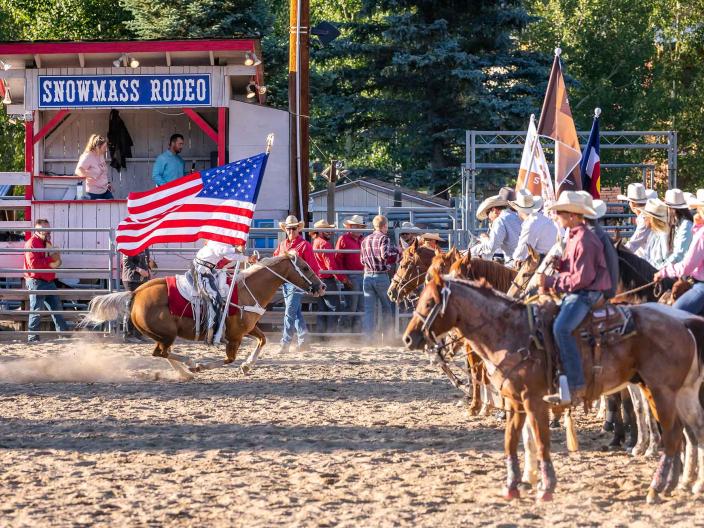 people carrying flags ride horses at rodeo