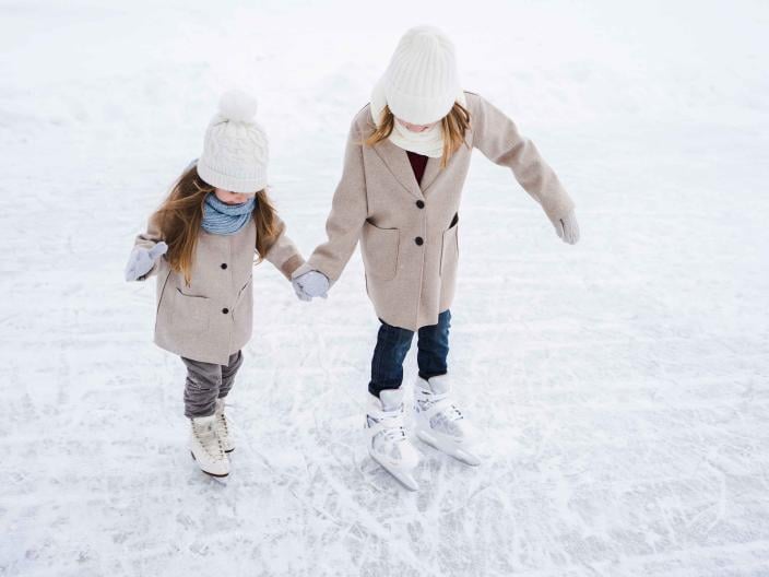 two people in white hats and peacoats skate on frozen lake