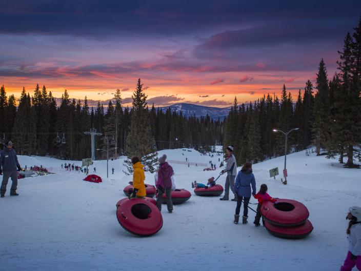 group of people holding tubes stand on snow as sunsets