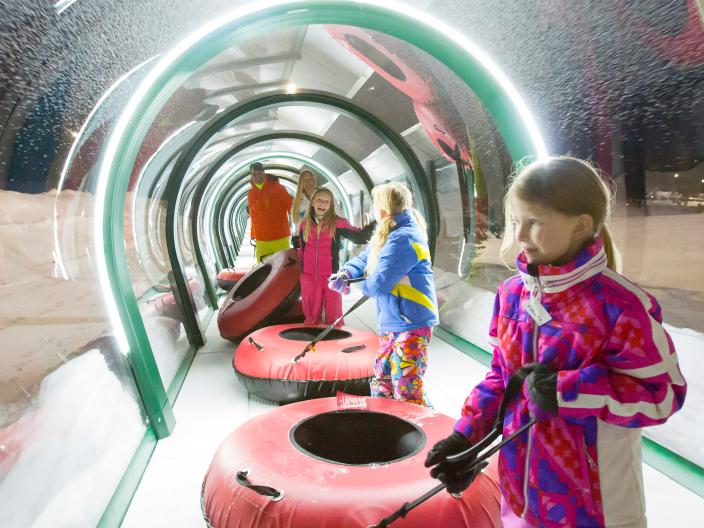 group of children holding tubes walk through an enclosed tube