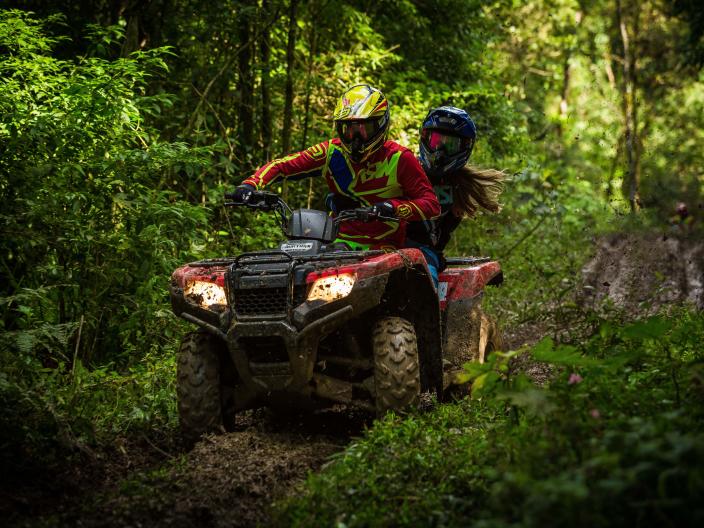 two people on ATV wearing helmets drive through forest