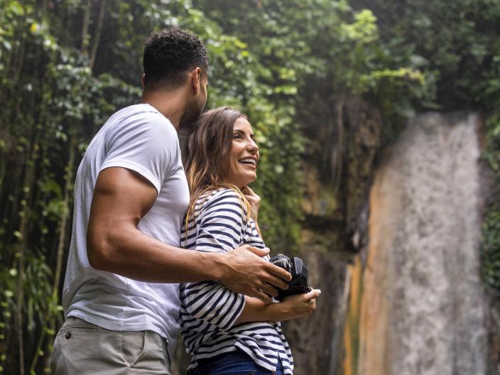 couple carrying a camera stand in front of waterfall