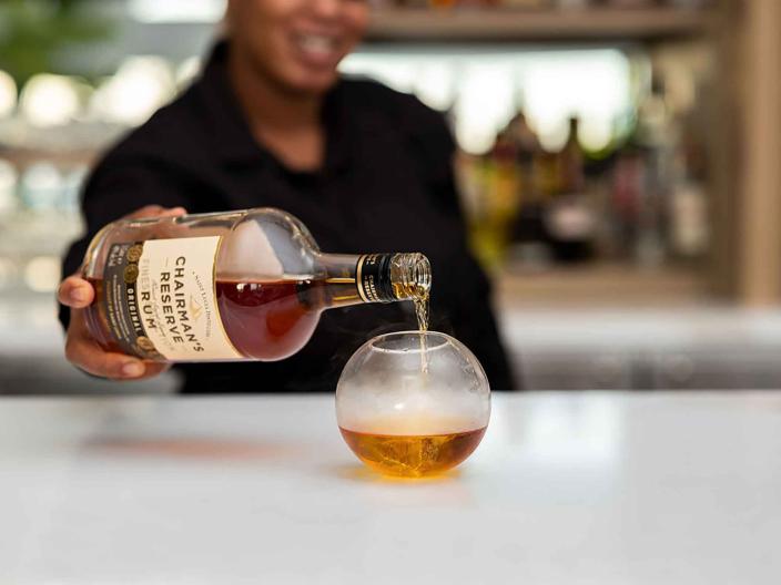 person pouring rum into circular glass on counter