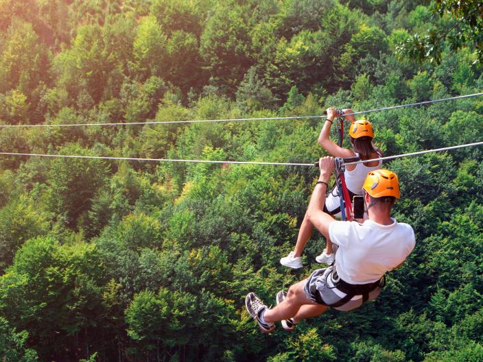 two people wearing orange helmets on zipline through forest