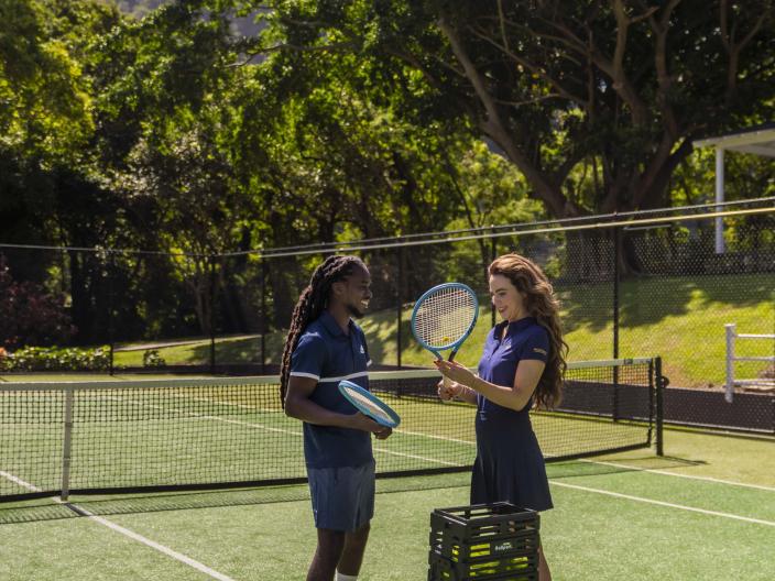 two people speak on a court while holding paddles