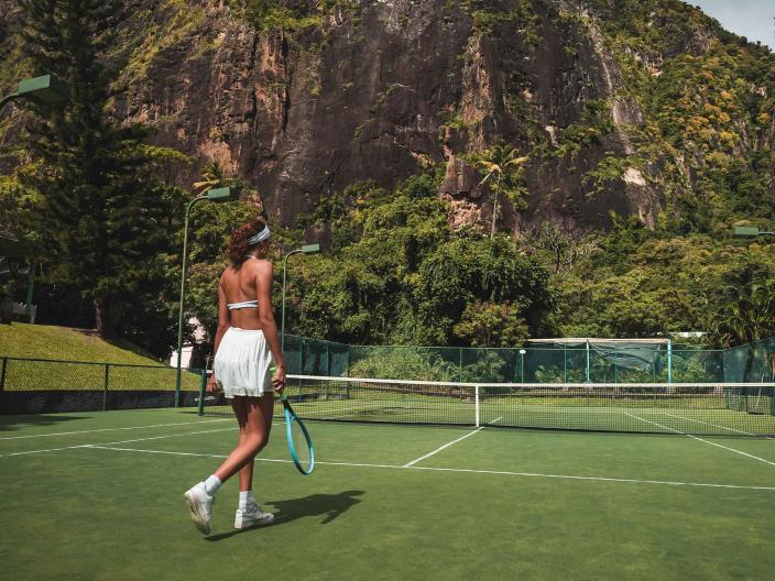 woman in white tennis outfit on tennis court with mountain in background