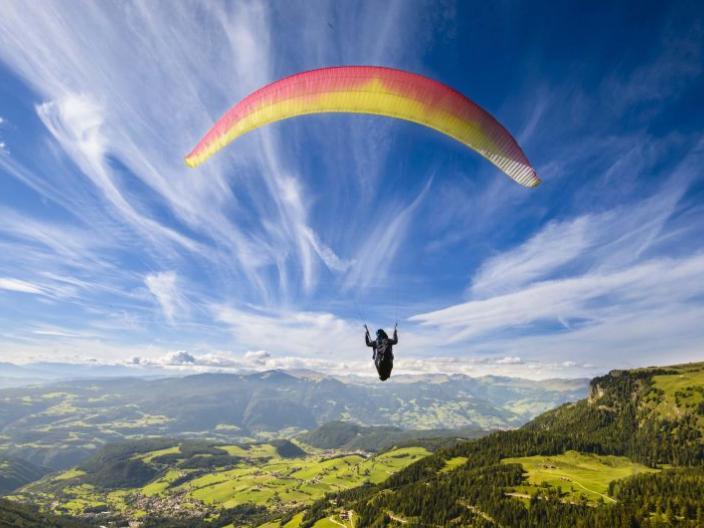 Hang gliding in the mountains with a blue sky streaked in clouds.