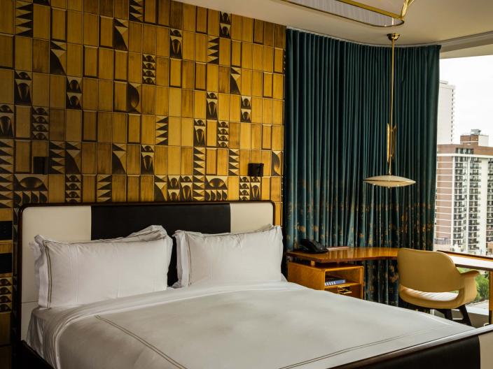 A hip hotel room at Viceroy Chicago, with a large bed and an accent wall made of textured gold panels