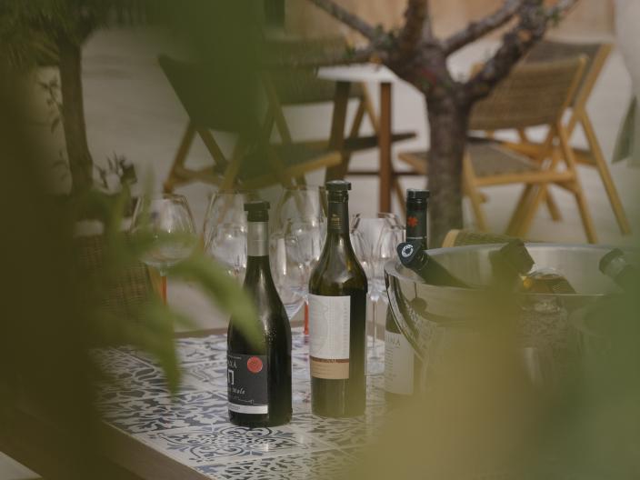 Wine bottles and glasses on a dining table, on an outdoor dining terrace lined with trees