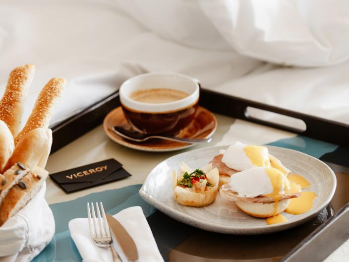 A breakfast tray on a bed, with an egg sandwich and a coffeee