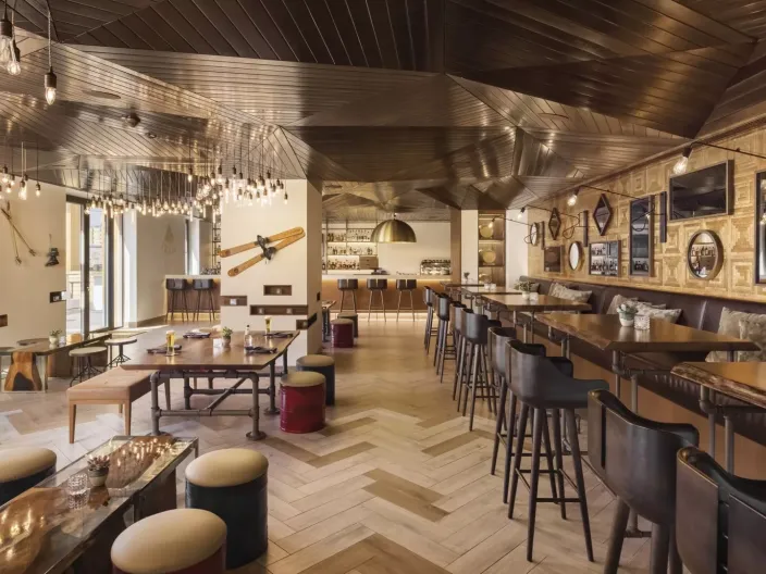 The dining room of Pique Ski Bar, with a long bar, several tables and ski paraphenalia decorating the ceiling