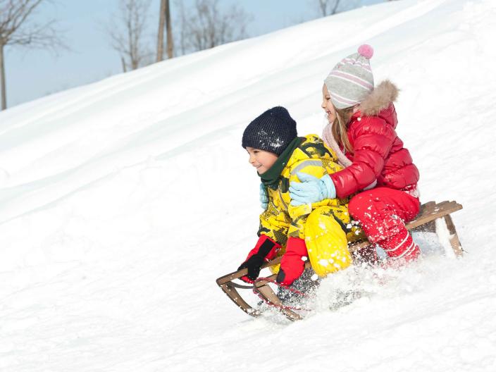 Two small children descend a small hill in a wooden sled